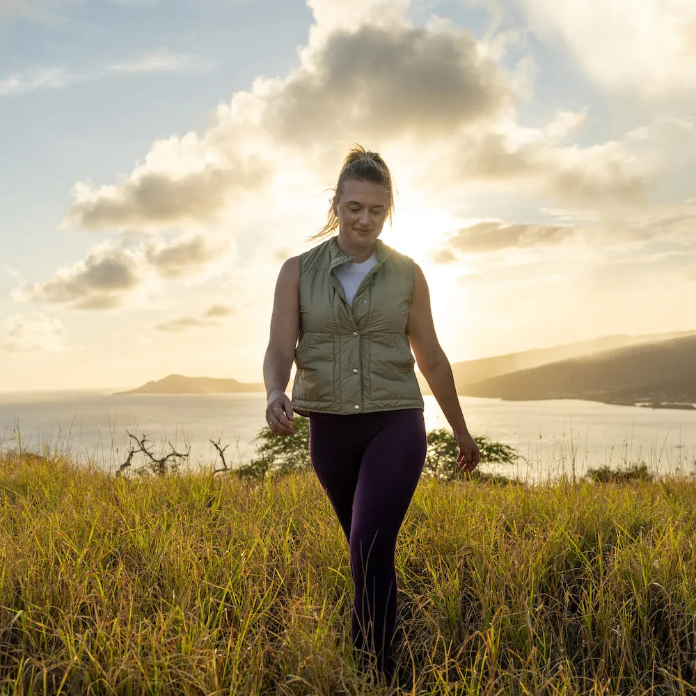 Woman walking in a field with a scenic background of mountains and water.