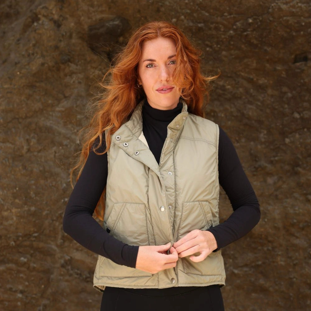 Woman wearing a green vest against a brown stone wall